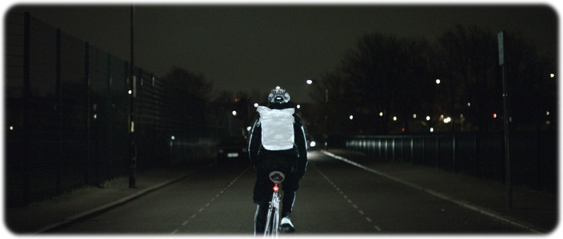 A single cyclist riding at night with the life paint on his bike,shoes,helmet and backpack