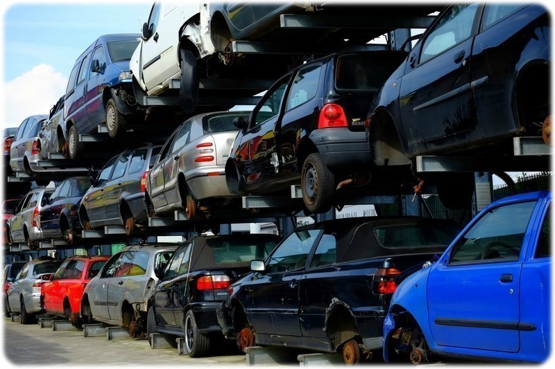 Scrapyard picture containing scrap cars staked on each other, all damaged and missing various parts